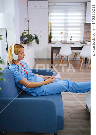 Nurse relaxing on sofa listening music and using tablet after work at home Nurse relaxing on sofa listening music and using tablet after work at home 140356211