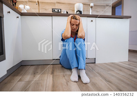 Exhausted doctor sitting on the floor in the kitchen after work 140356232