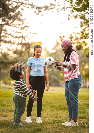 Family playing soccer outdoors in park during golden hour 140356243