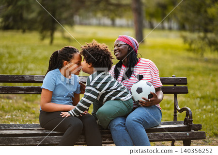 Mother and children bonding on park bench with soccer ball Mother and children bonding on park bench with soccer ball 140356252