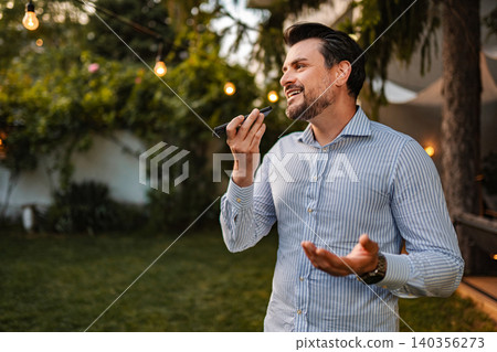 Man talking on speaker phone in garden at evening Man talking on speaker phone in garden at evening 140356273