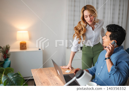 Couple collaborating on home office laptop and smartphone Couple collaborating on home office laptop and smartphone 140356332