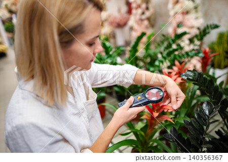 Young botanist inspecting plants with magnifying glass in greenhouse Young botanist inspecting plants with magnifying glass in greenhouse 140356367