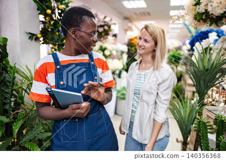 Florist showing plants to customer using digital tablet in flower shop Florist showing plants to customer using digital tablet in flower shop 140356368