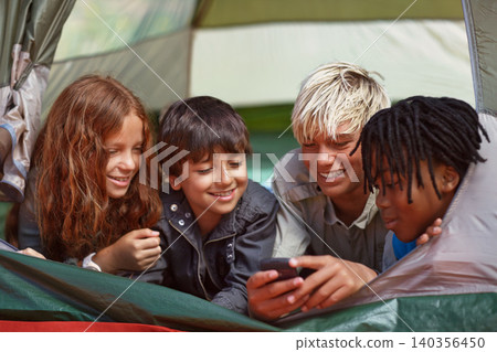 Phone, happy and children in tent for camp networking on social media, mobile app or internet. Smile, technology and young kids bonding, relax and streaming video online with cellphone on vacation. Phone, happy and children in tent for camp networking on social media, mobile app or internet. Smile, technology and young kids bonding, relax and streaming video online with cellphone on vacation. 140356450
