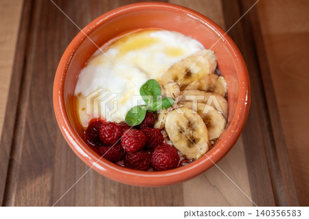 Delicious yogurt bowl topped with fresh raspberries and bananas in a cozy cafe Delicious yogurt bowl topped with fresh raspberries and bananas in a cozy cafe 140356583