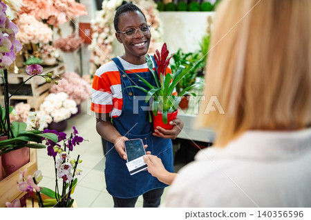 Florist smiling and accepting a contactless payment from a customer in a flower shop Florist smiling and accepting a contactless payment from a customer in a flower shop 140356596