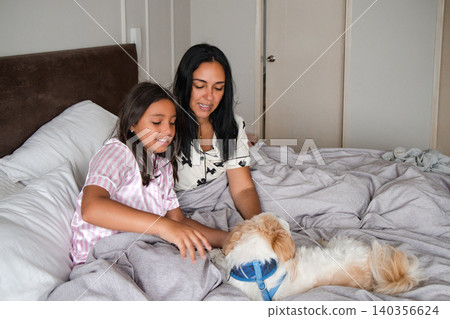 A woman and a girl are laying on a bed with a dog A woman and a girl are laying on a bed with a dog 140356624