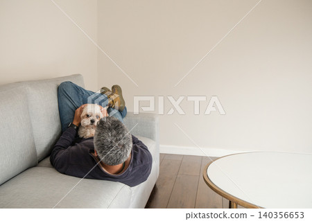 A man is laying on a couch with a dog on his lap 140356653