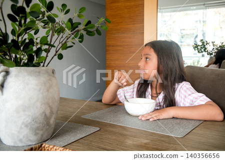 A girl is eating cereal at a table A girl is eating cereal at a table 140356656