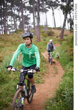 Woman, bike and cycling outdoor on trail for exercise, workout or adventure in forest with fitness. People, cyclists and bicycle with helmet in woods or off road for sport, hobby and travel in nature 140357008