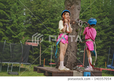 Children are standing on the bridge, putting on a sports helmet and preparing to pass obstacles at the height of the suspended rope town. 140357054
