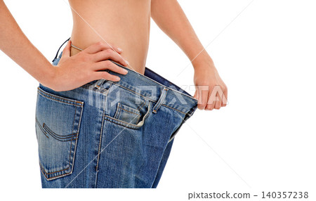 Diet, wellness and woman with big pants in studio for weight loss, fitness or exercise results. Health, body and closeup of female person with jeans for measuring slim stomach by white background. Diet, wellness and woman with big pants in studio for weight loss, fitness or exercise results. Health, body and closeup of female person with jeans for measuring slim stomach by white background. 140357238