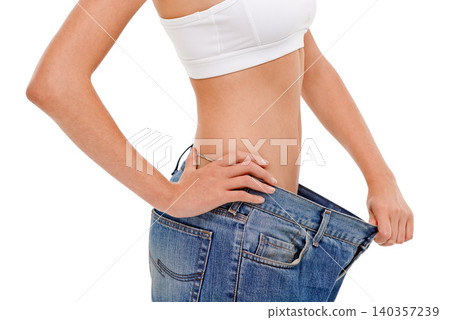 Diet, health and woman with big pants in studio for weight loss, fitness or exercise results. Wellness, body and closeup of female person with jeans for measuring slim stomach by white background. Diet, health and woman with big pants in studio for weight loss, fitness or exercise results. Wellness, body and closeup of female person with jeans for measuring slim stomach by white background. 140357239