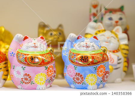 Kanazawa, Japan - Oct 6 2024, A close-up view of white cat and maneki-neko figurines decorated with various colorful flower and dot patterns on a shelf in a souvenir shop of Kanazawa, Japan Kanazawa, Japan - Oct 6 2024, A close-up view of white cat and maneki-neko figurines decorated with various colorful flower and dot patterns on a shelf in a souvenir shop of Kanazawa, Japan 140358366