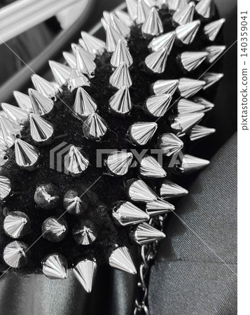 Closeup view of spiked accessory of metal and fabric. Spikes arranged in pattern, with mix textures. Dark background, shiny silver of spikes. Part of fashion accessory or clothing detail Closeup view of spiked accessory of metal and fabric. Spikes arranged in pattern, with mix textures. Dark background, shiny silver of spikes. Part of fashion accessory or clothing detail 140359041