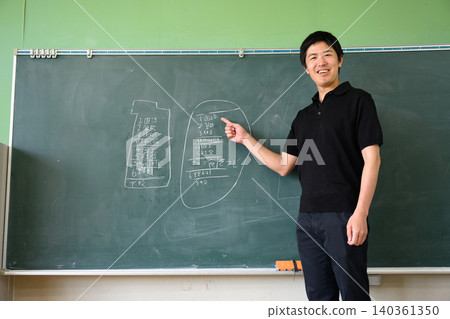 一位身穿polo衫的男老師面帶微笑,指著教室黑板上的課表。 一位身穿polo衫的男老師面帶微笑,指著教室黑板上的課表。 140361350
