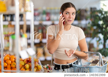 Woman with phone in hands walks around store, call to friend, speak with mother Woman with phone in hands walks around store, call to friend, speak with mother 140361999