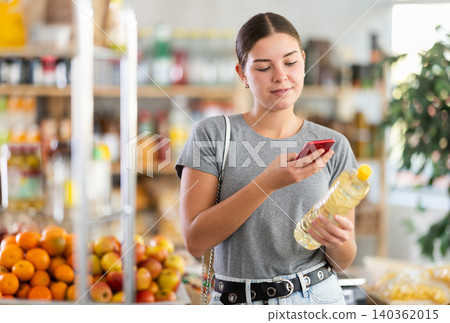 In shop youth girl scan QR code and take reading vegetable oil package bottle using phone camera In shop youth girl scan QR code and take reading vegetable oil package bottle using phone camera 140362015