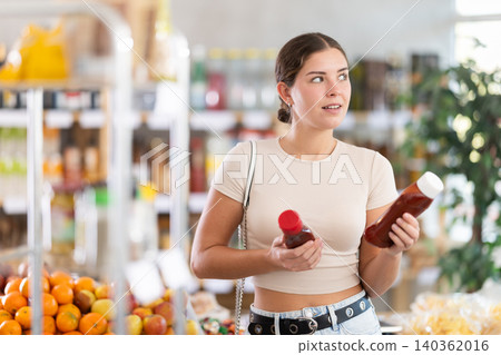 Girl hold bottle, choose and buy ketchup in store 140362016