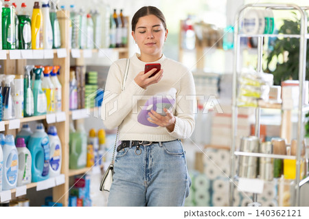 Before making purchase, young woman buyer scans QR code on packaging of liquid detergent 140362121