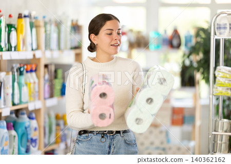 Young woman housewife in household store examines package, chooses toilet paper. 140362162