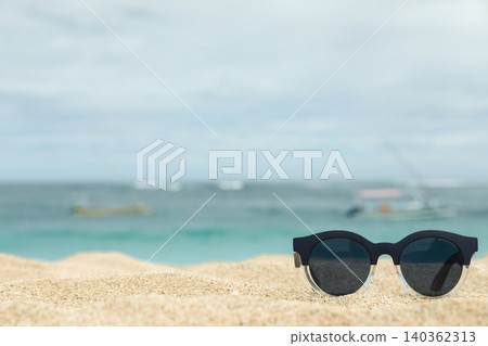 Sunglasses are on sand with ocean and boats in Bali Sunglasses are on sand with ocean and boats in Bali 140362313