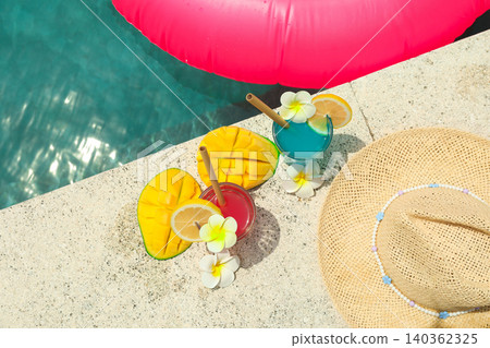 Two drinks sit by the pool near a straw hat and fruit Two drinks sit by the pool near a straw hat and fruit 140362325