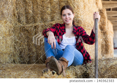 Portrait of a young positive farmer girl resting on haystacks Portrait of a young positive farmer girl resting on haystacks 140362383