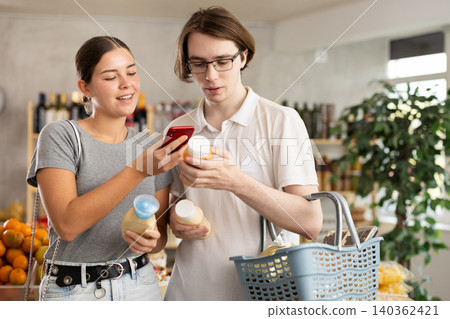 In shop youth girl and guy scan QR code and take reading sauce package bottle using phone camera In shop youth girl and guy scan QR code and take reading sauce package bottle using phone camera 140362421