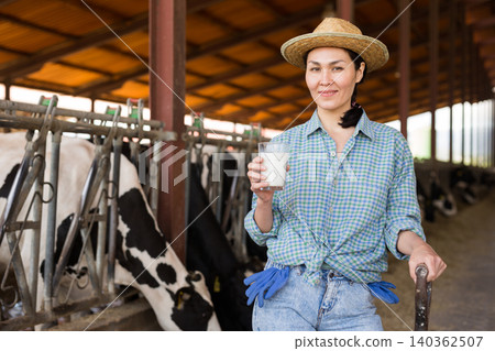 Portrait of a positive kazakh farmer woman in a cowshed, holding a glass of milk Portrait of a positive kazakh farmer woman in a cowshed, holding a glass of milk 140362507