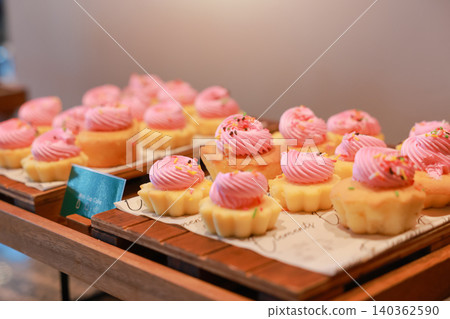 Freshly baked mini cupcakes with pink buttercream frosting and colorful sprinkles arranged on wooden trays at a luxury hotel dessert buffet. Sweet bakery pastry for morning brunch catering display. Freshly baked mini cupcakes with pink buttercream frosting and colorful sprinkles arranged on wooden trays at a luxury hotel dessert buffet. Sweet bakery pastry for morning brunch catering display. 140362590