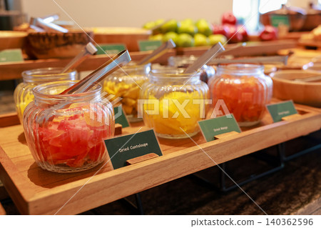 Close up of colorful dried fruits like cantaloupe and mango in glass jars with serving tongs on a wooden tray at a luxury hotel breakfast buffet. Healthy sweet snack for morning catering display. Close up of colorful dried fruits like cantaloupe and mango in glass jars with serving tongs on a wooden tray at a luxury hotel breakfast buffet. Healthy sweet snack for morning catering display. 140362596
