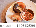 Partially eaten chocolate frosted donut with colorful sprinkles and a messy empty small bowl of chocolate cream spread on a white plate. Sweet leftover dessert food after breakfast meal at a cafe. 140362599