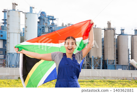 Happy young woman worker with flag of South Africa against background of factory Happy young woman worker with flag of South Africa against background of factory 140362881