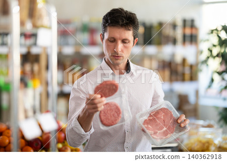 Man in light shirt choose and buy raw cooled beef entrecote and hamburger cutlet in store Man in light shirt choose and buy raw cooled beef entrecote and hamburger cutlet in store 140362918