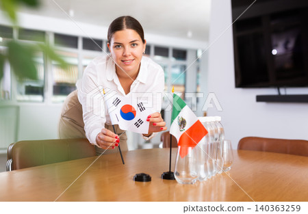 Woman secretary prepares an office for negotiations - she places flags of South Korea and Mexico table Woman secretary prepares an office for negotiations - she places flags of South Korea and Mexico table 140363259
