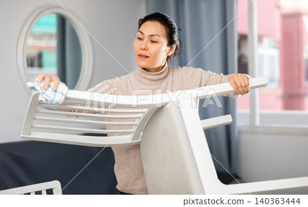 Asian woman wipes a chair with a damp cloth Asian woman wipes a chair with a damp cloth 140363444