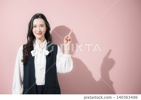 An image of a female receptionist with a pink background, pointing and smiling at the camera while introducing or recommending something. An image of a female receptionist with a pink background, pointing and smiling at the camera while introducing or recommending something. 140363486