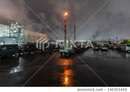 A factory night view with a flare stack and rain-soaked road in Chidori-cho, Kawasaki City. A factory night view with a flare stack and rain-soaked road in Chidori-cho, Kawasaki City. 140363488