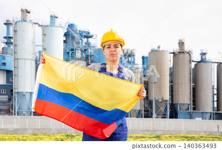 Portrait of upset girl in construction overalls with the Colombia flag on the background of modern factory Portrait of upset girl in construction overalls with the Colombia flag on the background of modern factory 140363493