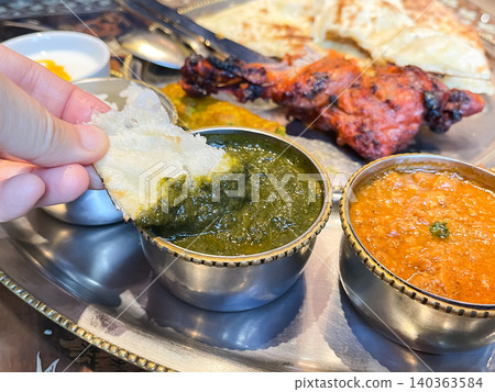 Spinach curry eaten at an Indian curry restaurant. A picture of someone eating the curry with naan bread. 140363584