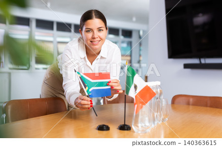 Young lady sets miniatures flags of Mexico and South Africa for international negotiations 140363615