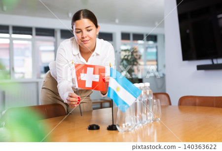 Positive young woman putting little flag of Switzerland on table next to the flag of Argentina Positive young woman putting little flag of Switzerland on table next to the flag of Argentina 140363622