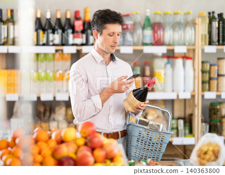 Man in light shirt scan QR code and take reading wine using phone camera in shop Man in light shirt scan QR code and take reading wine using phone camera in shop 140363800