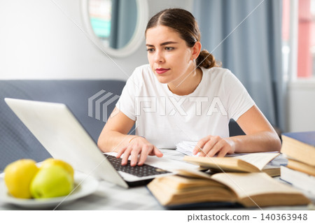 Woman studying via internet using laptop while sitting at table at home Woman studying via internet using laptop while sitting at table at home 140363948