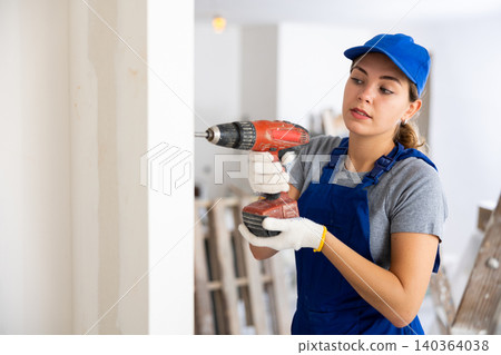 Young woman drilling a hole in the wall with screwdriver Young woman drilling a hole in the wall with screwdriver 140364038
