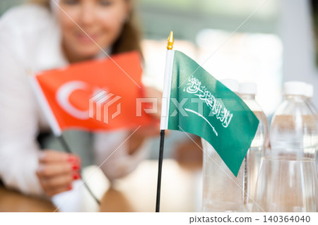 Woman secretary prepares an office for negotiations - she places flags of Saudi Arabia and Turkish table Woman secretary prepares an office for negotiations - she places flags of Saudi Arabia and Turkish table 140364040