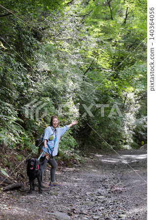 A woman smiles as she interacts with her dog in the forest, enjoying her outdoor lifestyle – a direct look at the camera. 140364056