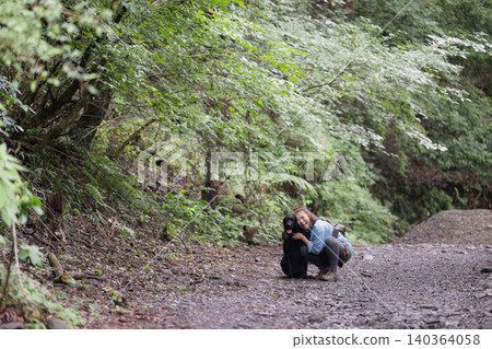A woman smiles as she interacts with her dog in the forest, enjoying her outdoor lifestyle – a direct look at the camera. 140364058
